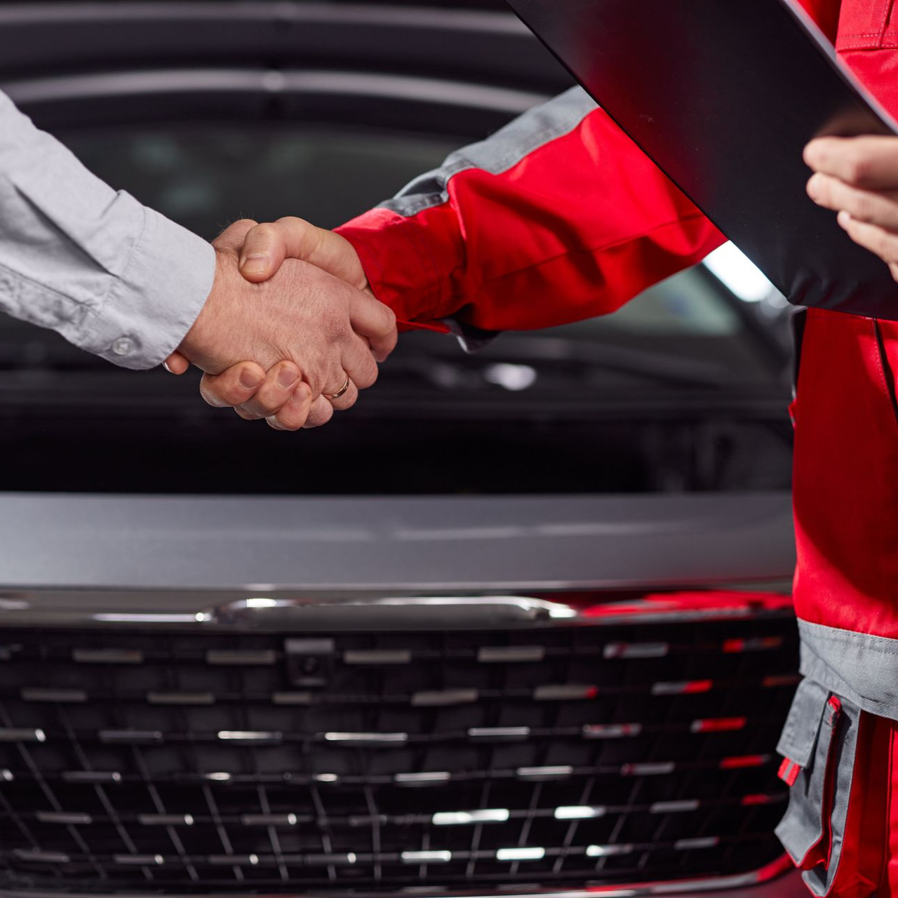 Deux personnes se serrent la main devant une voiture.