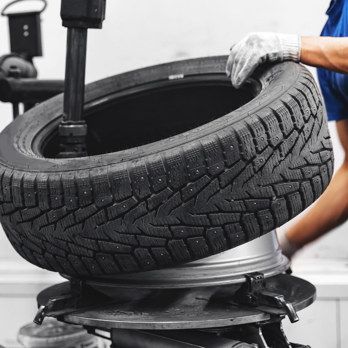 Une main gantée monte un pneu d'hiver noir sur une jante métallique à l'aide d'une machine.