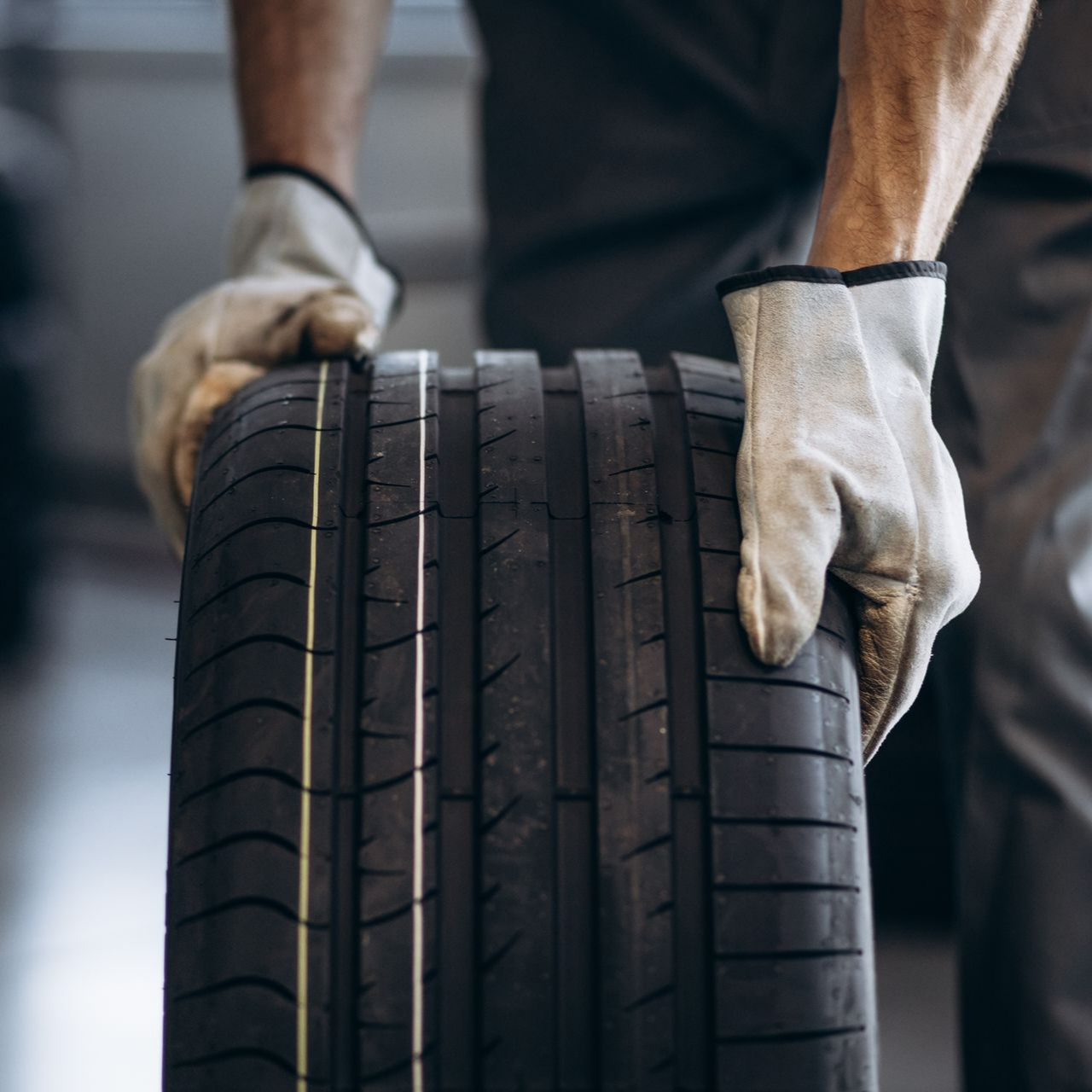 Une personne portant des gants de travail tient un pneu neuf.