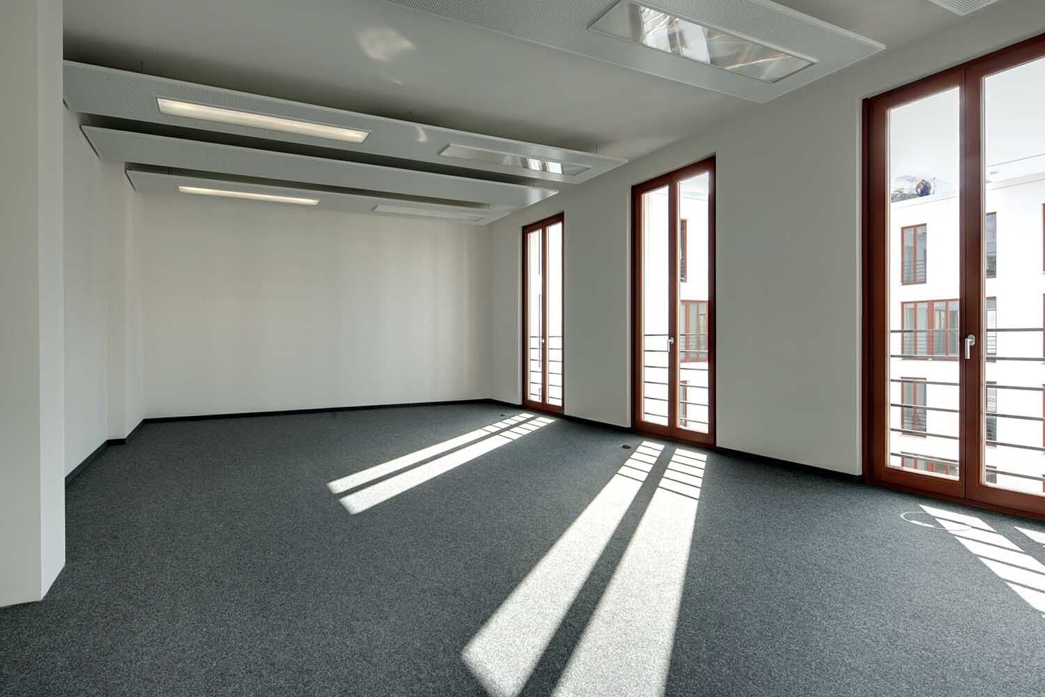 Pièce comprenant trois portes-fenêtres et recouverte de moquette grise