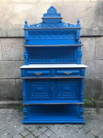 Gabinete antiguo azul con tallas ornamentales y encimera de mármol contra una pared de piedra.