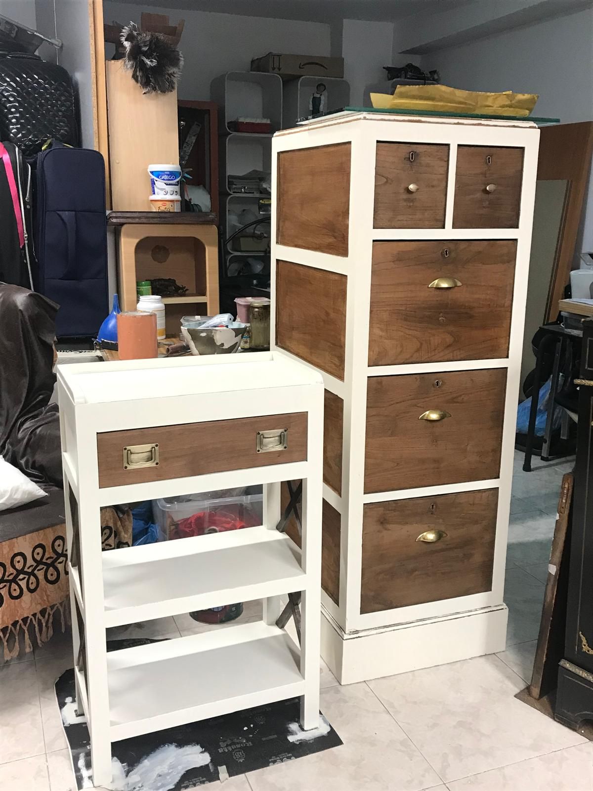 Dos armarios de madera, uno alto con cajones y otro bajo con cajón y estantes, pintados de blanco y teñidos de marrón.