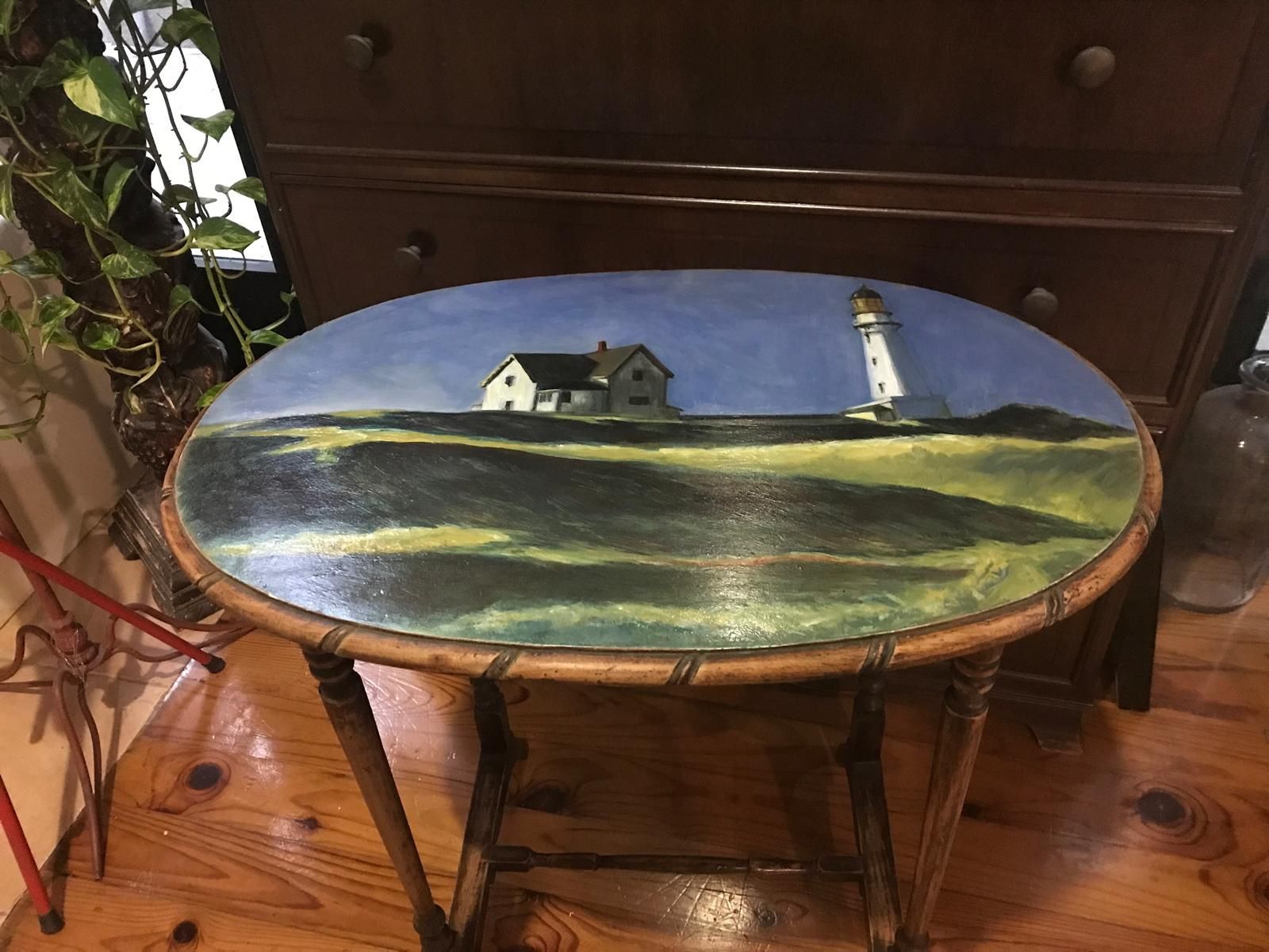 Mesa ovalada con pintura de faro en la parte superior; marco de madera marrón.