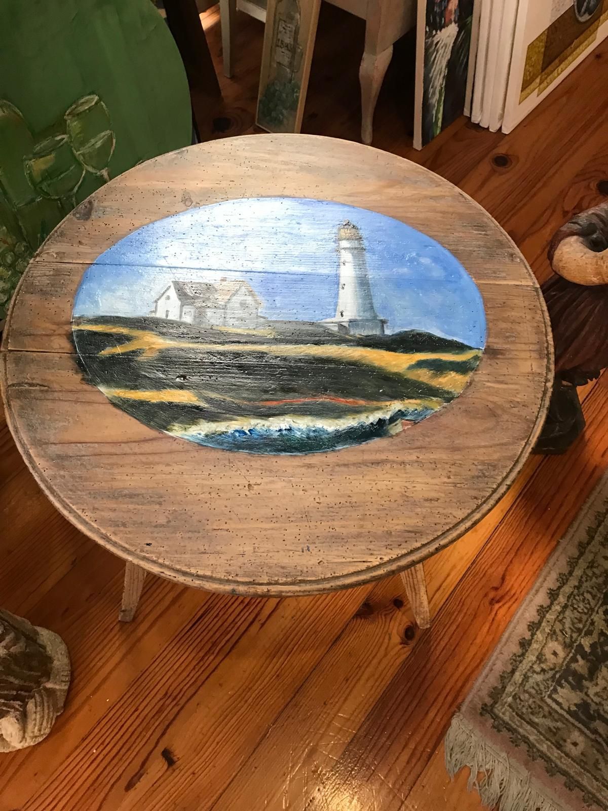 Mesa auxiliar de madera con escena de faro pintado: edificio blanco, cielo azul, océano y madera marrón.
