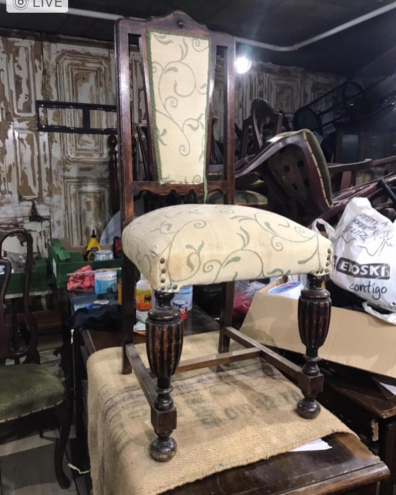 Silla antigua de madera con tela floral en una habitación desordenada.