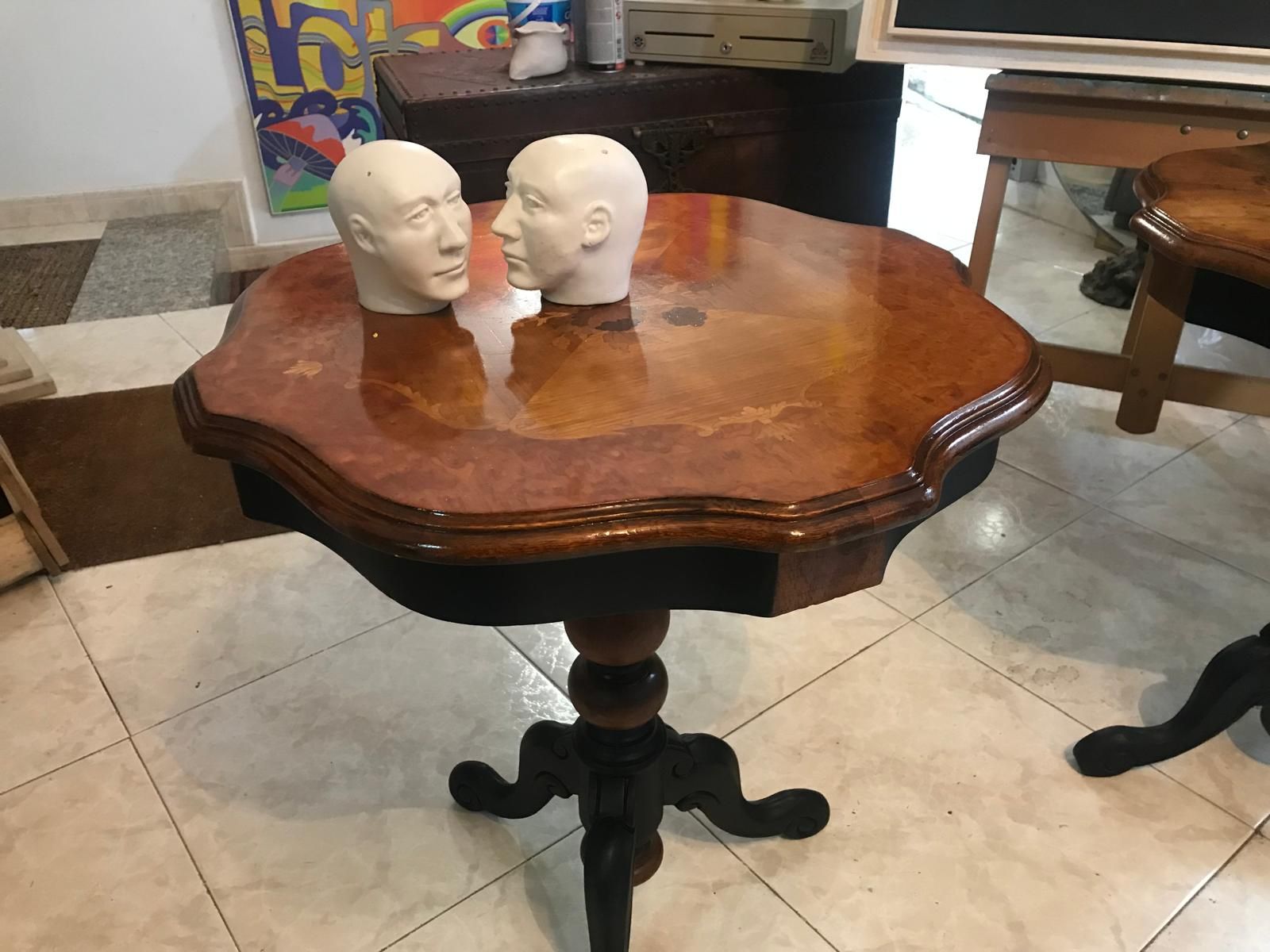 Dos cabezas de maniquí blancas sobre una mesa de madera oscura, con una base de pedestal ornamentada, en el interior.
