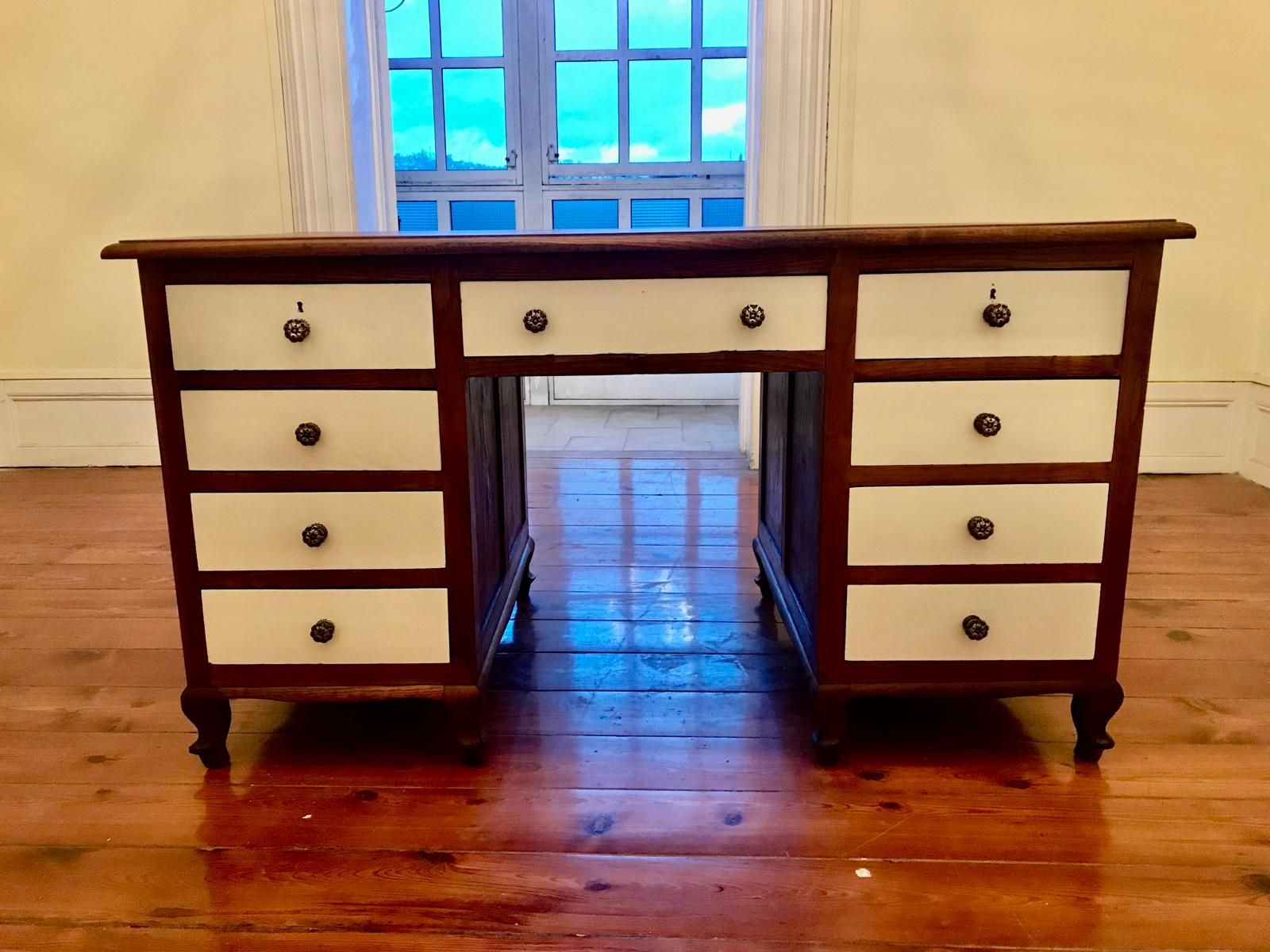 Un escritorio de madera con frentes de cajones blancos y una ventana al fondo.