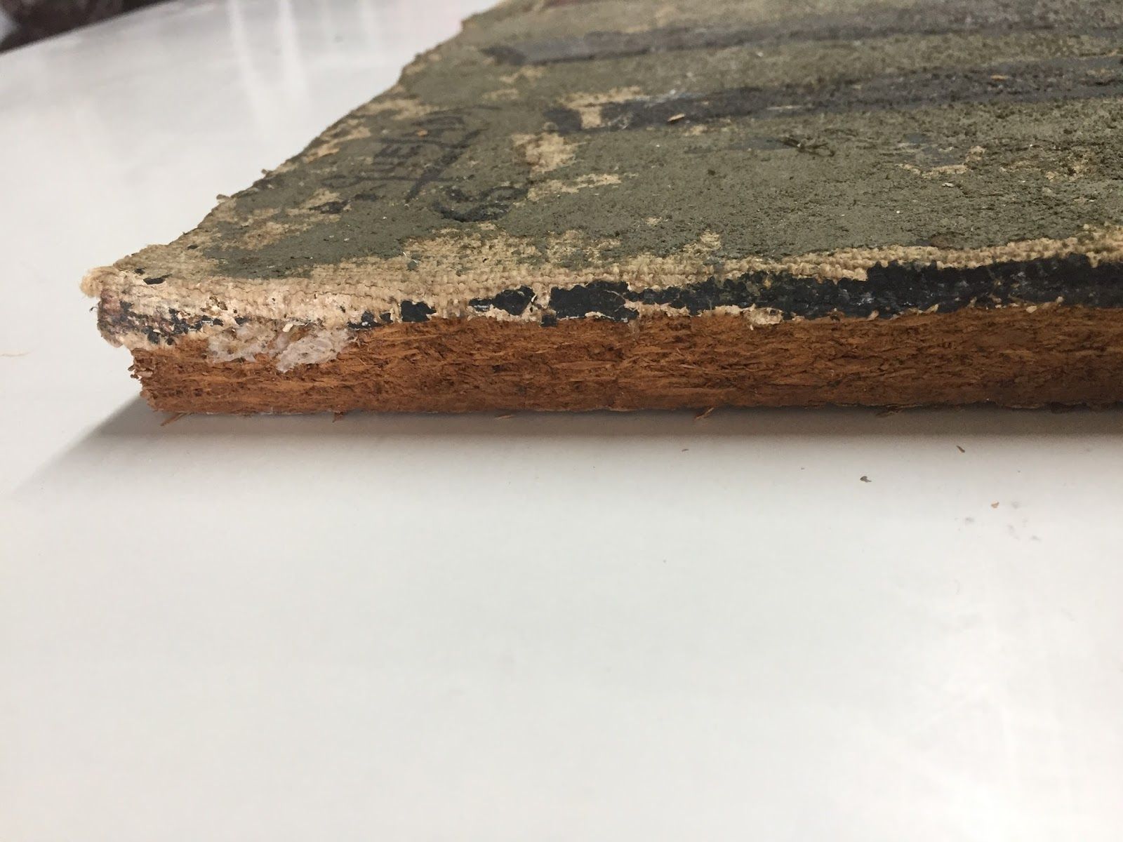 Un objeto cuadrado y en capas, posiblemente alimento, muestra una parte superior verde mohosa, una capa negra y una base marrón.