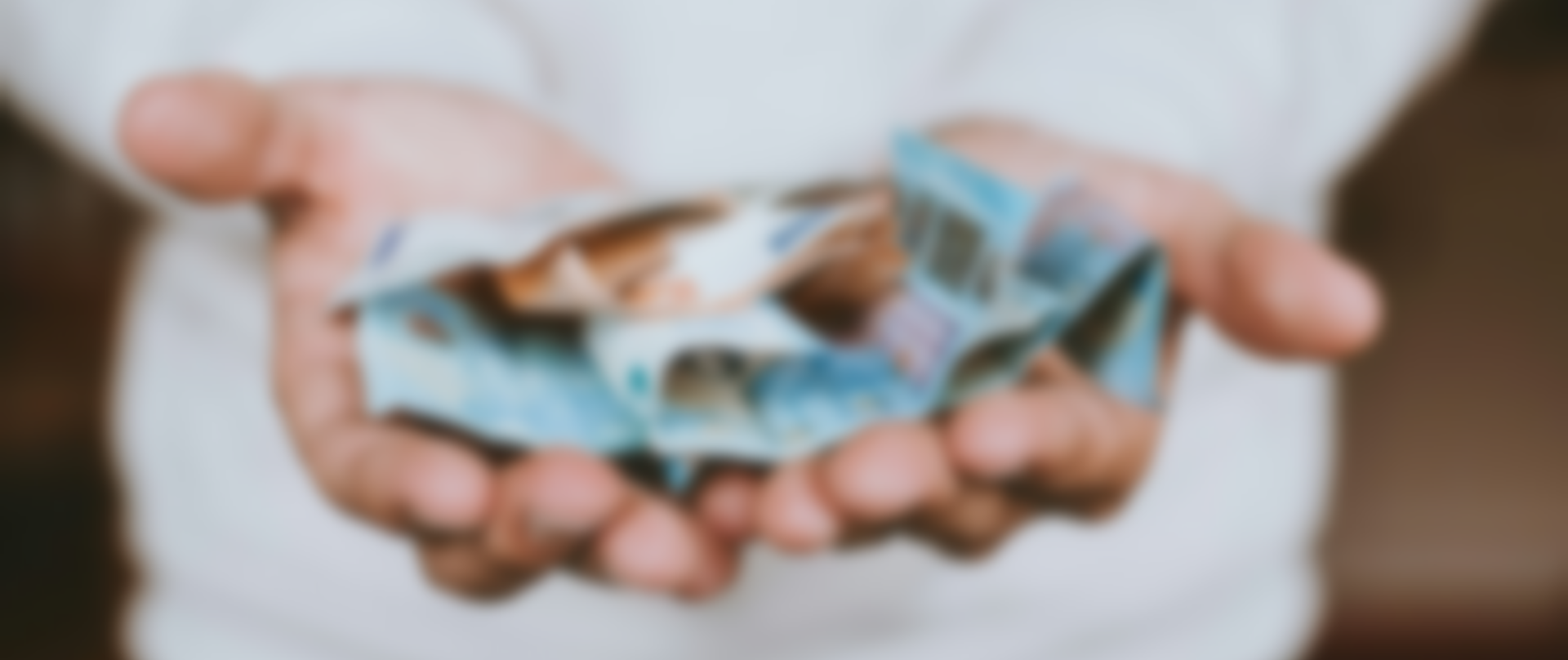 Ein Paar schalenförmig geformte Hände halten einen kleinen Stapel blauer Geldscheine.