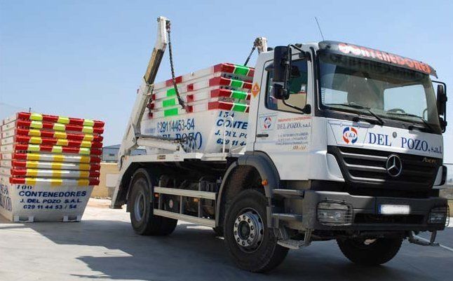 Un camión volquete Mercedes está estacionado junto a una pila de contenedores de basura.