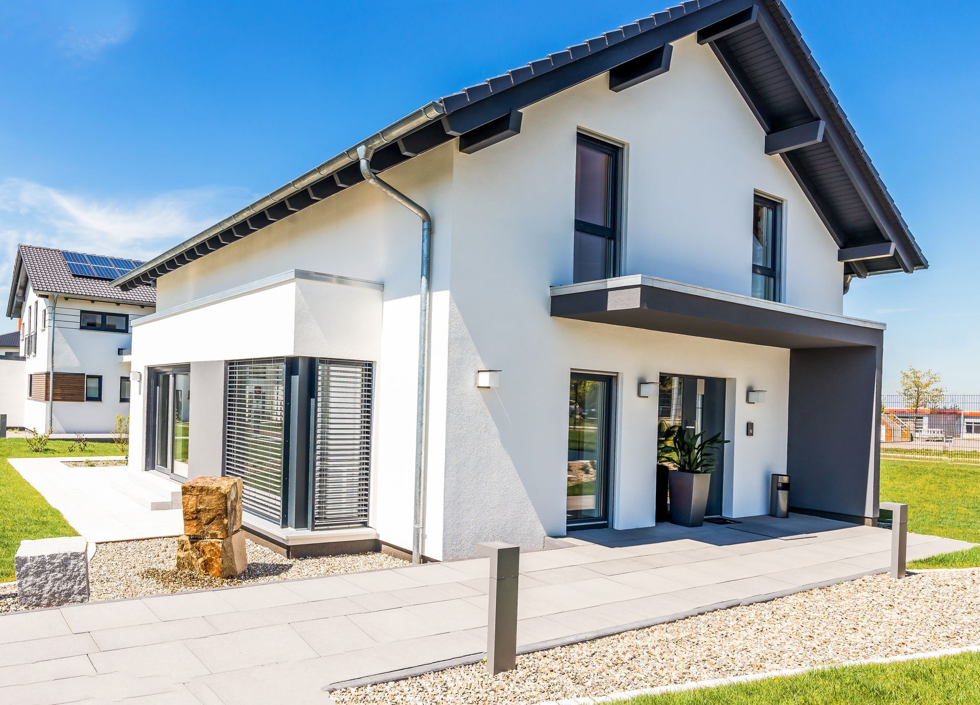 Maison moderne à deux étages avec extérieur blanc, garnitures noires, grandes fenêtres et une cour paysagée par une journée ensoleillée.