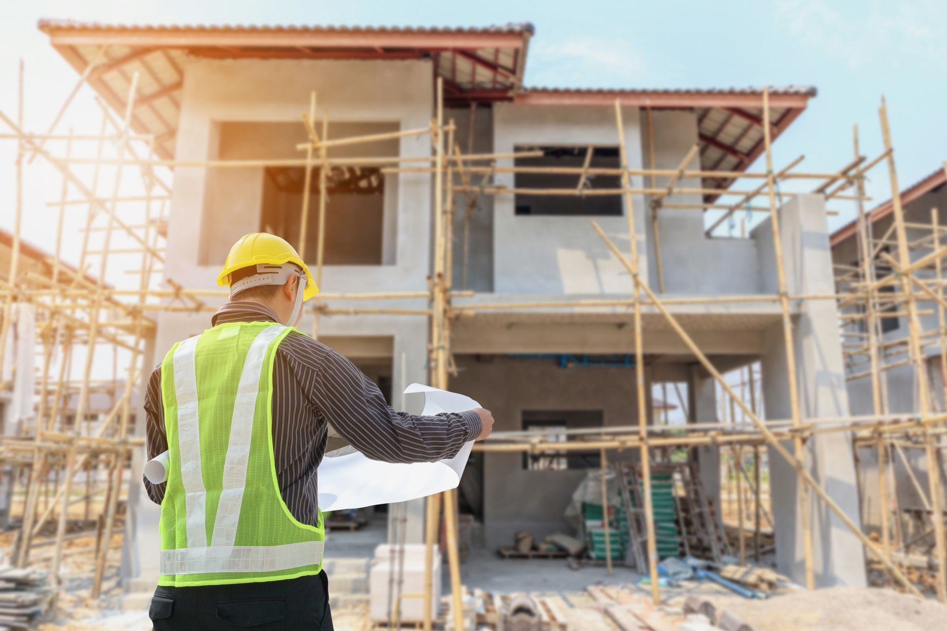 Un ouvrier du bâtiment portant un casque et un gilet jaunes examine les plans d'une maison en construction.