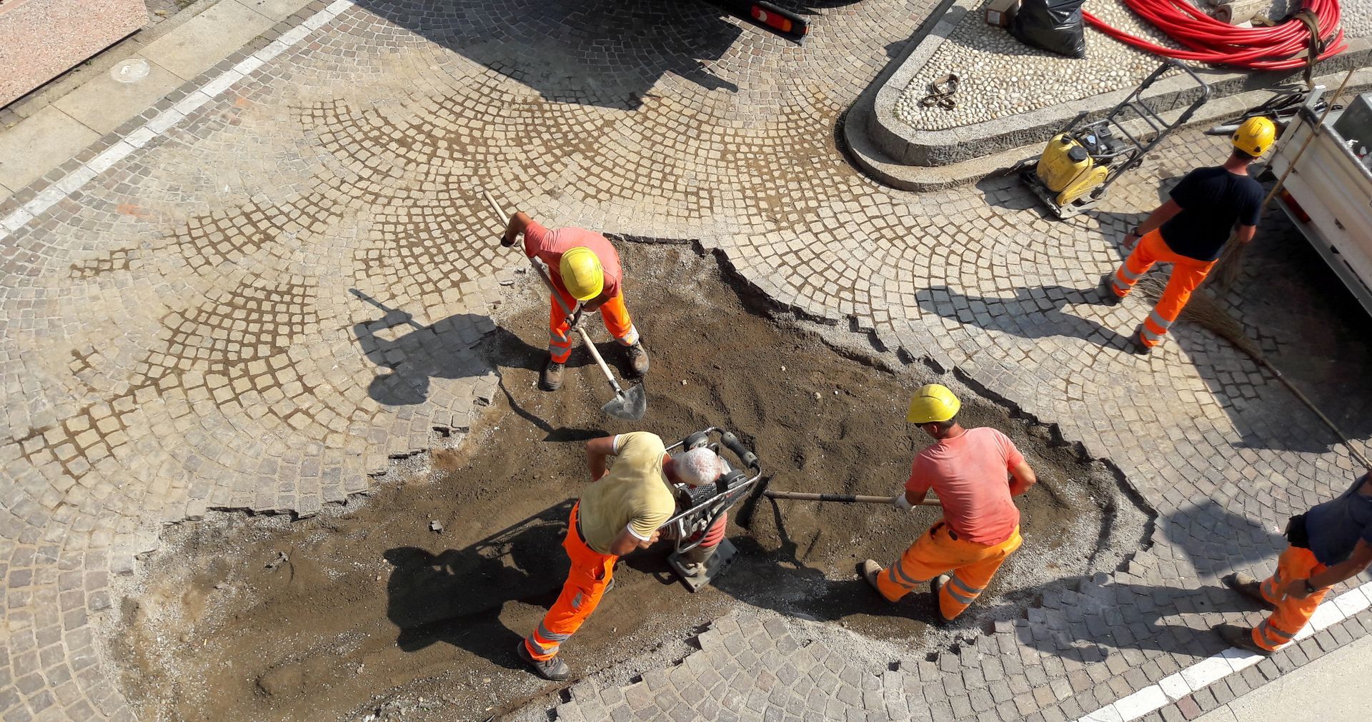Des ouvriers du bâtiment en uniforme orange et casques jaunes réparent une route endommagée.