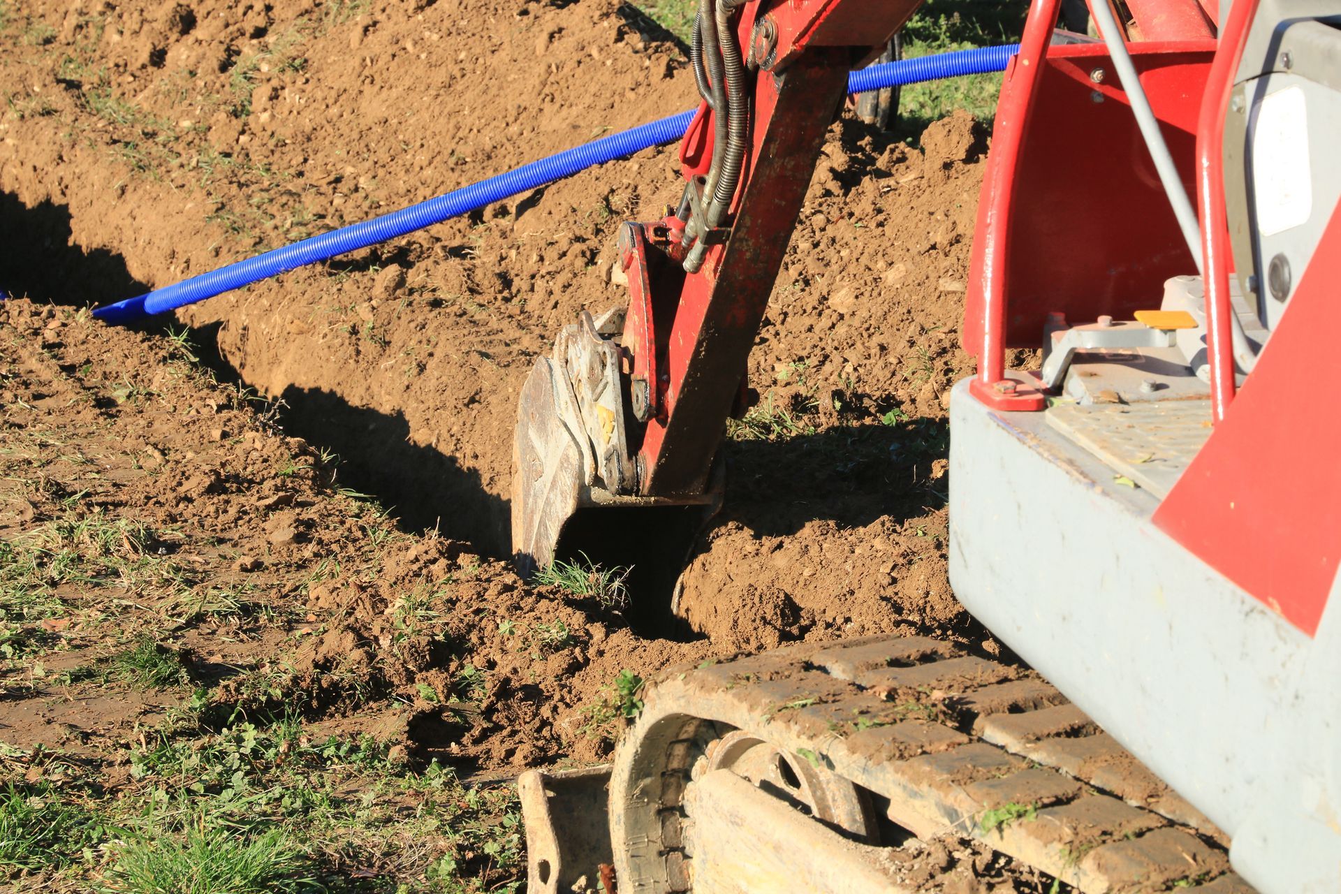 Minipelle creusant une tranchée à côté d'un tuyau bleu dans un champ de terre.