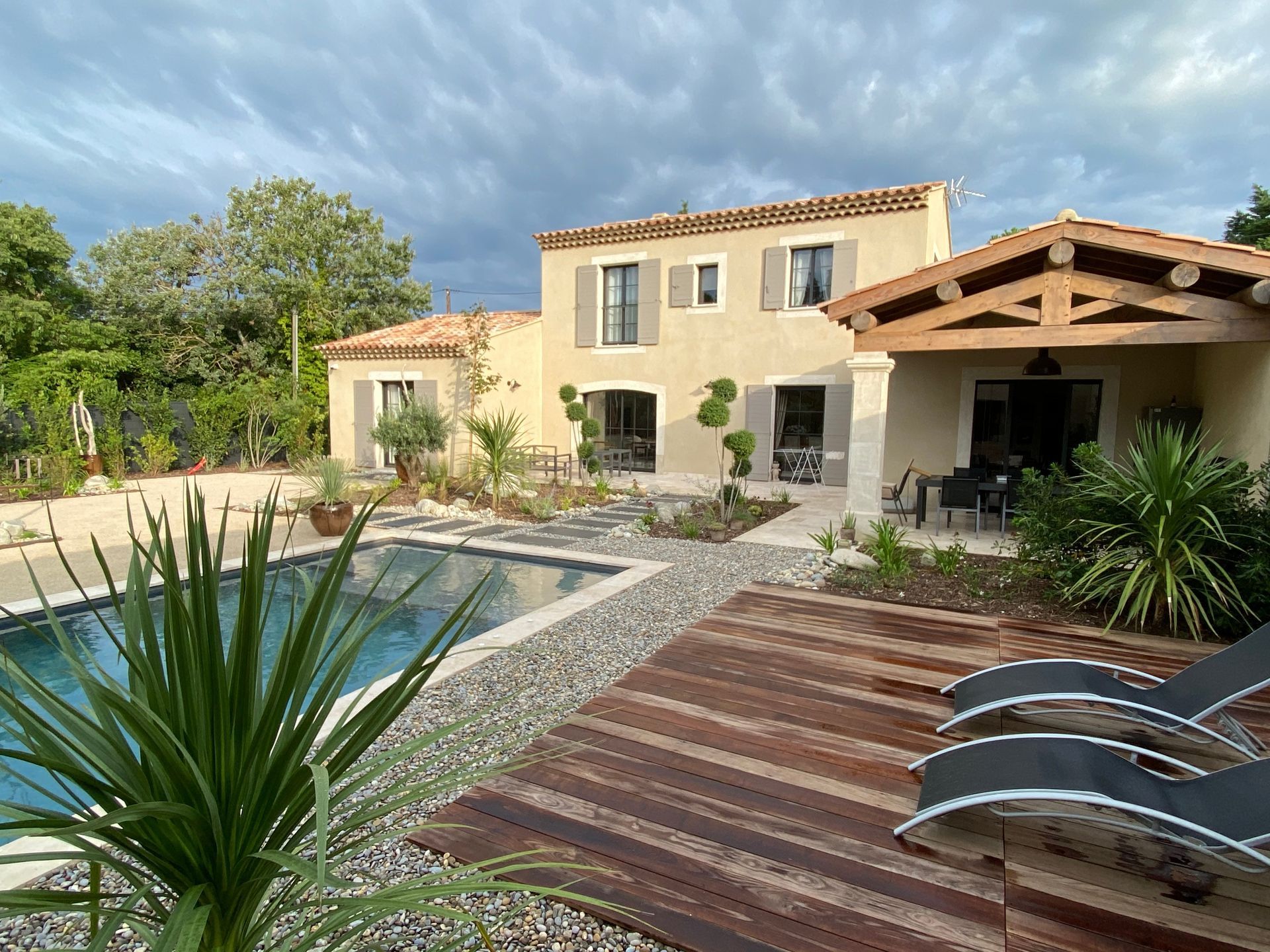 Une maison à deux étages avec piscine et terrasse en bois. Ciel couvert.
