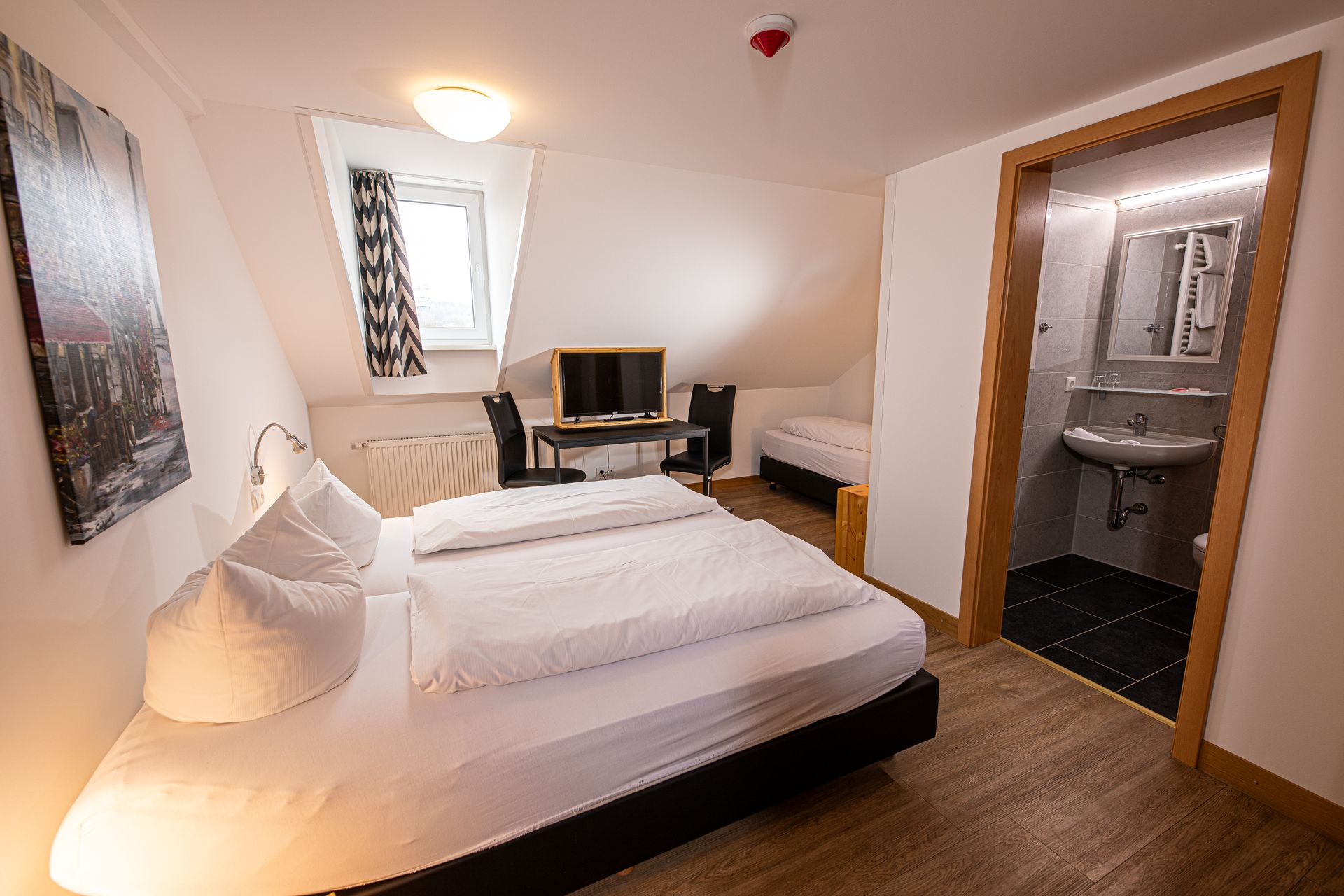 Gemütliches kleines Hotelzimmer mit Dachschräge, drei Betten und kleinem Schreibtisch im Gasthof Lamm.