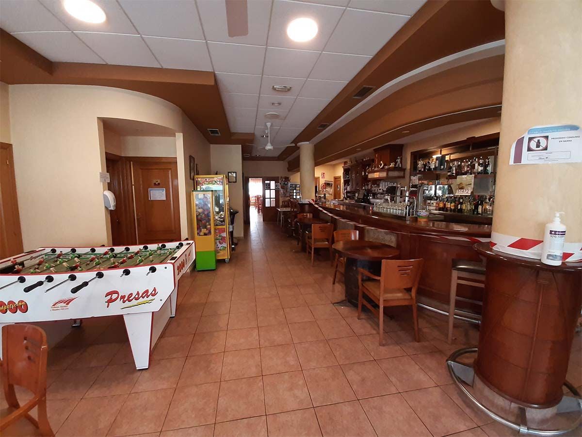 Interior de un bar con mesa de futbolín, juego de arcade, barra de madera y asientos.