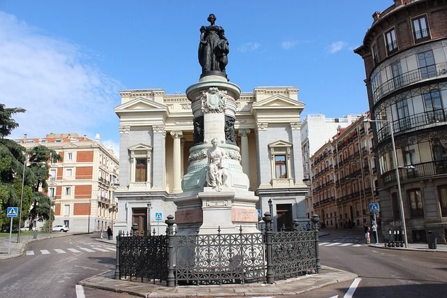 Estatua de la reina Isabel II en Madrid, España, frente a un edificio neoclásico, en un día soleado.