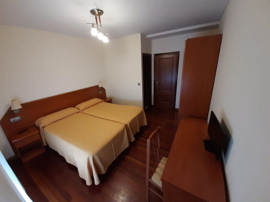 Habitación de hotel con dos camas individuales, escritorio, armario y puerta de madera cerrada.