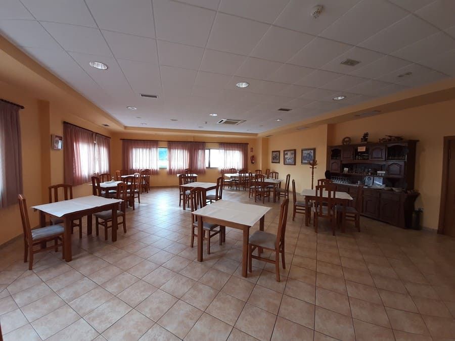 Comedor vacío con mesas, sillas, ventanas y un armario de madera oscura.