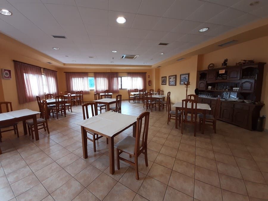 Comedor con mesas y sillas, ventanas con cortinas y mueble de madera.