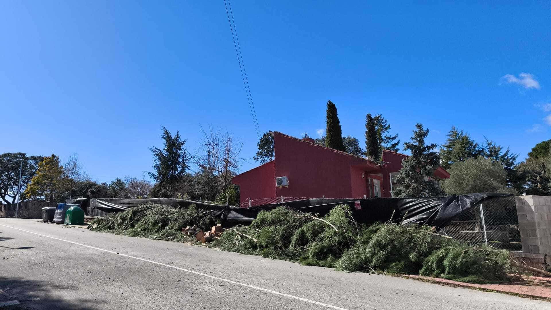 Casa roja en una ladera junto a una carretera, con árboles y arbustos bajo un cielo azul despejado.