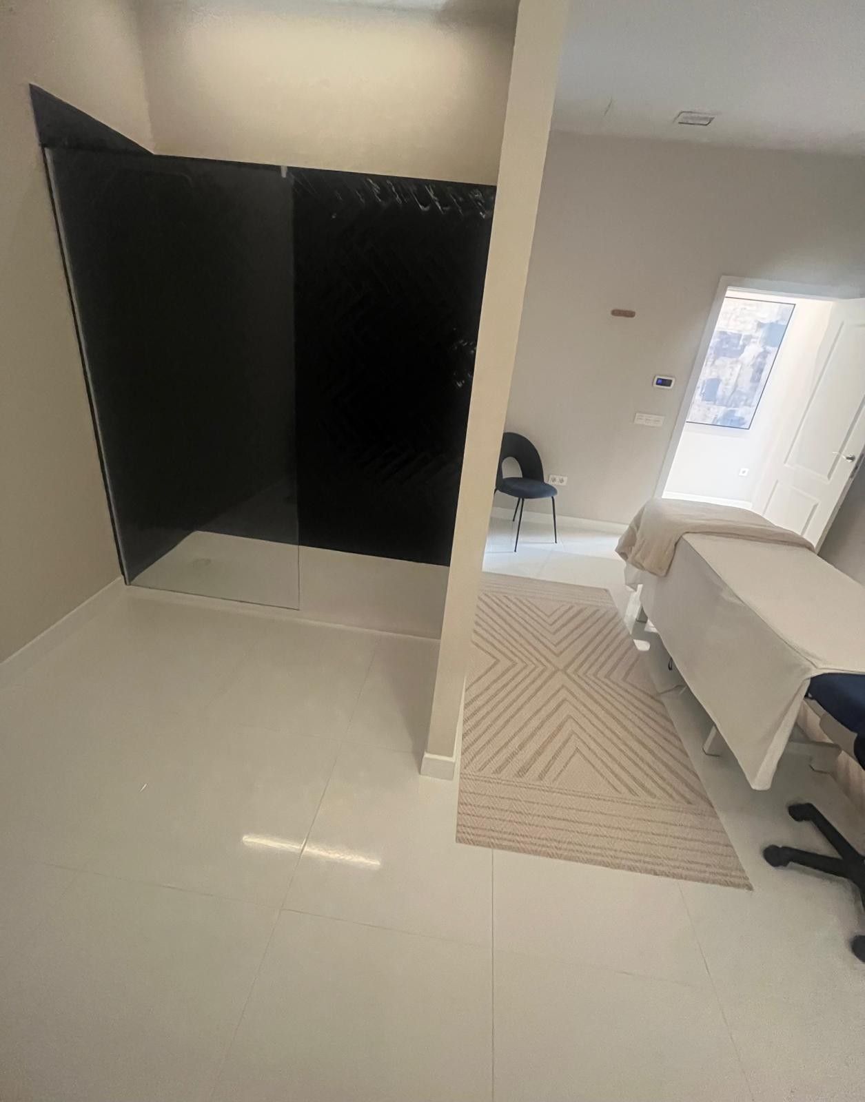 Salón moderno con dos sillas azules, una mesa pequeña y una lámpara de pared circular con luz tenue.