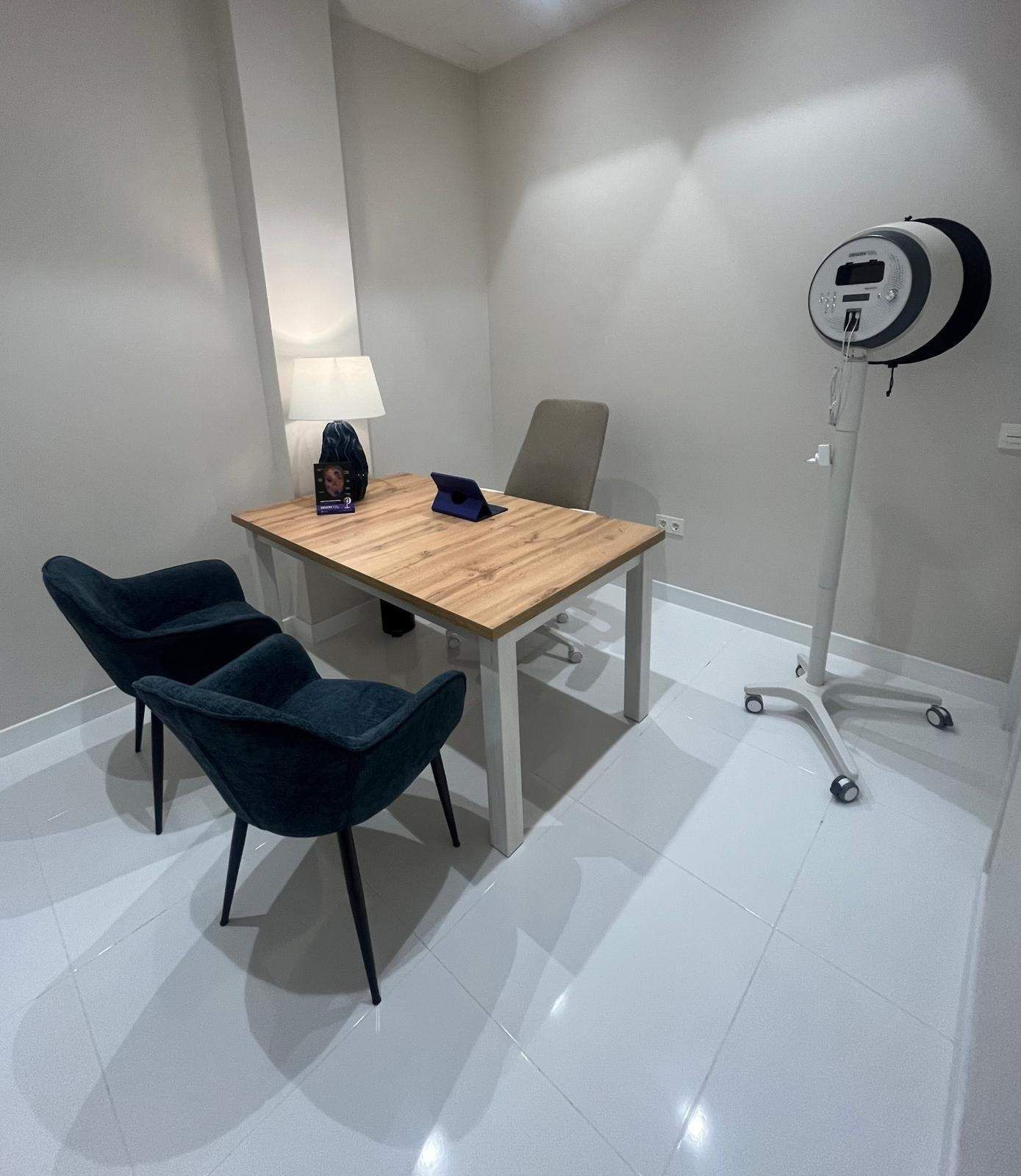 Pequeña sala de entrevistas con dos sillas, lámpara de escritorio y aro de luz sobre un soporte.