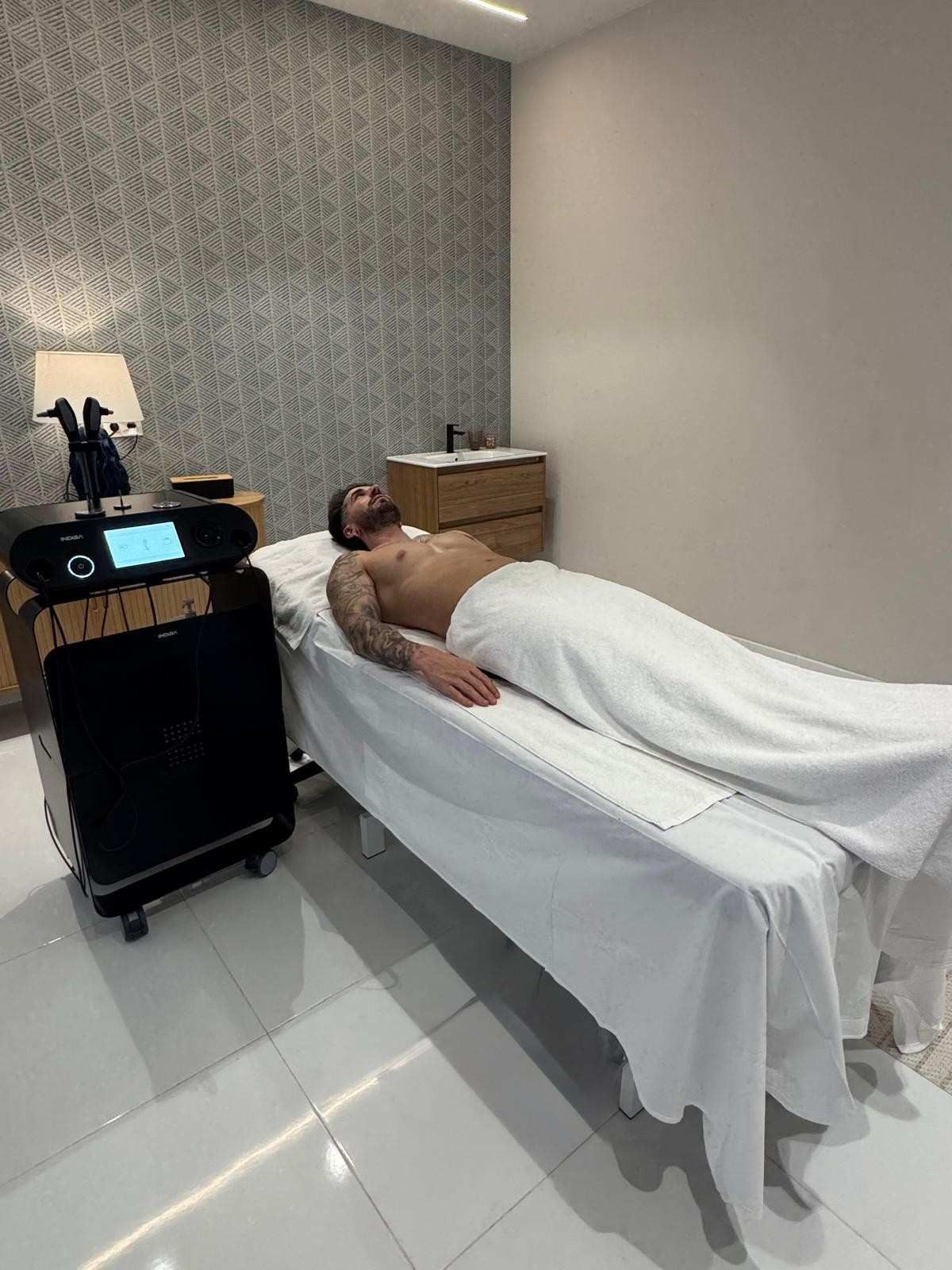 Masajista utilizando un dispositivo manual en la espalda de una persona en una sala de tratamiento luminosa.