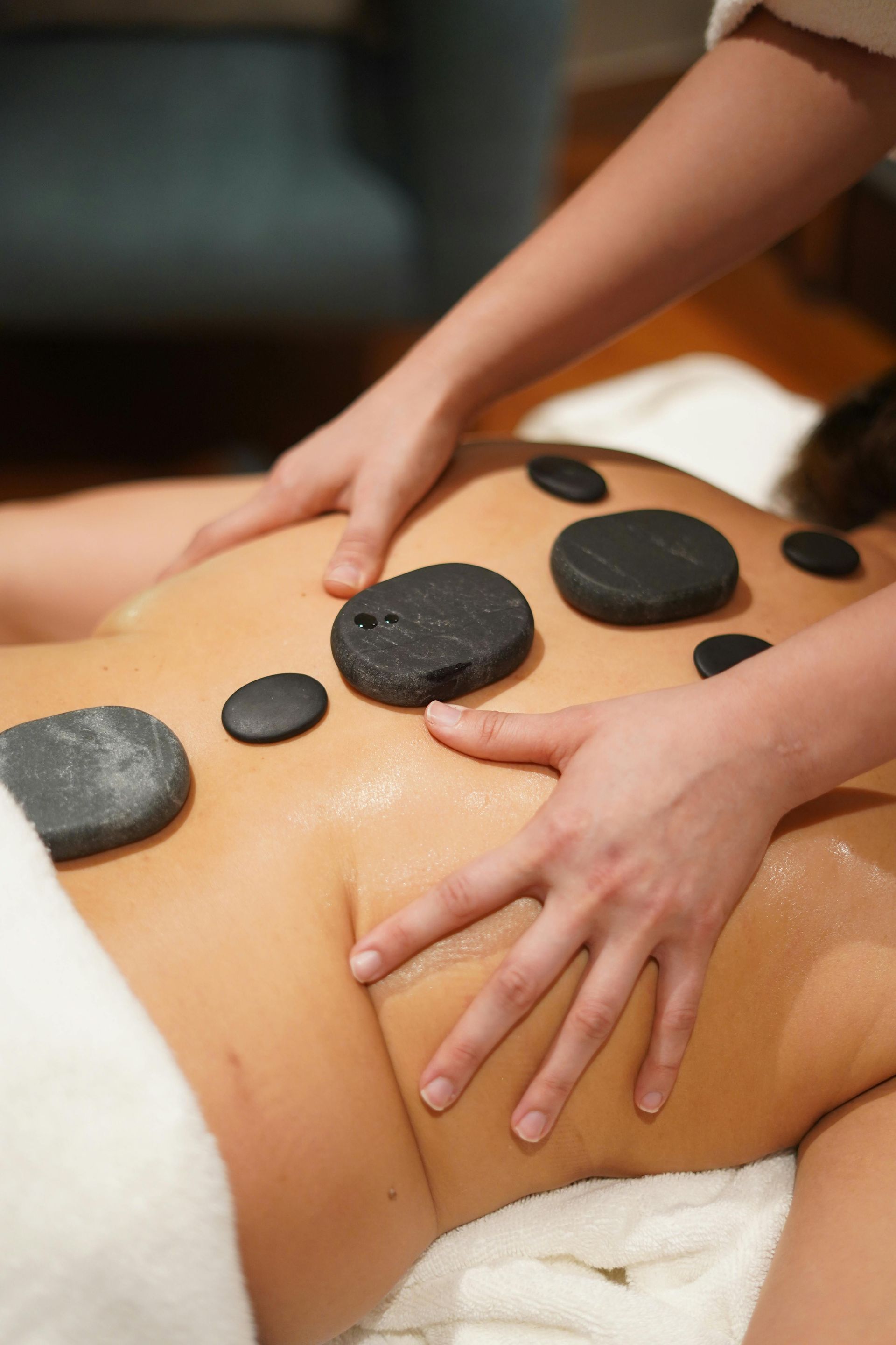 Masajista colocando piedras calientes sobre la espalda desnuda de un cliente durante un tratamiento de spa.