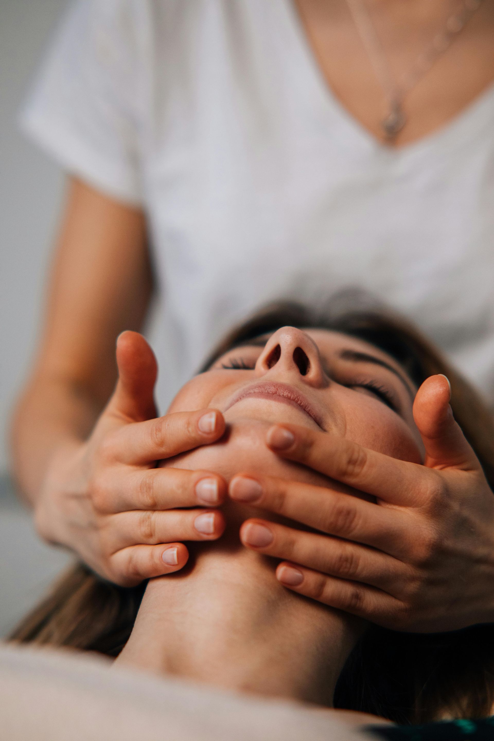 Persona recibiendo un masaje facial con las manos cubriendo las mejillas, en el interior de un edificio.