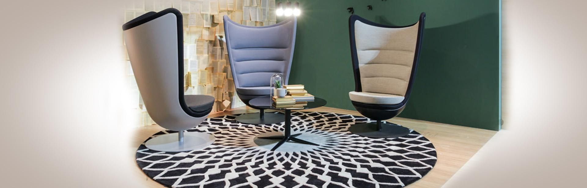 Tres sillas modernas con respaldo alto que rodean una mesa pequeña sobre una alfombra estampada.