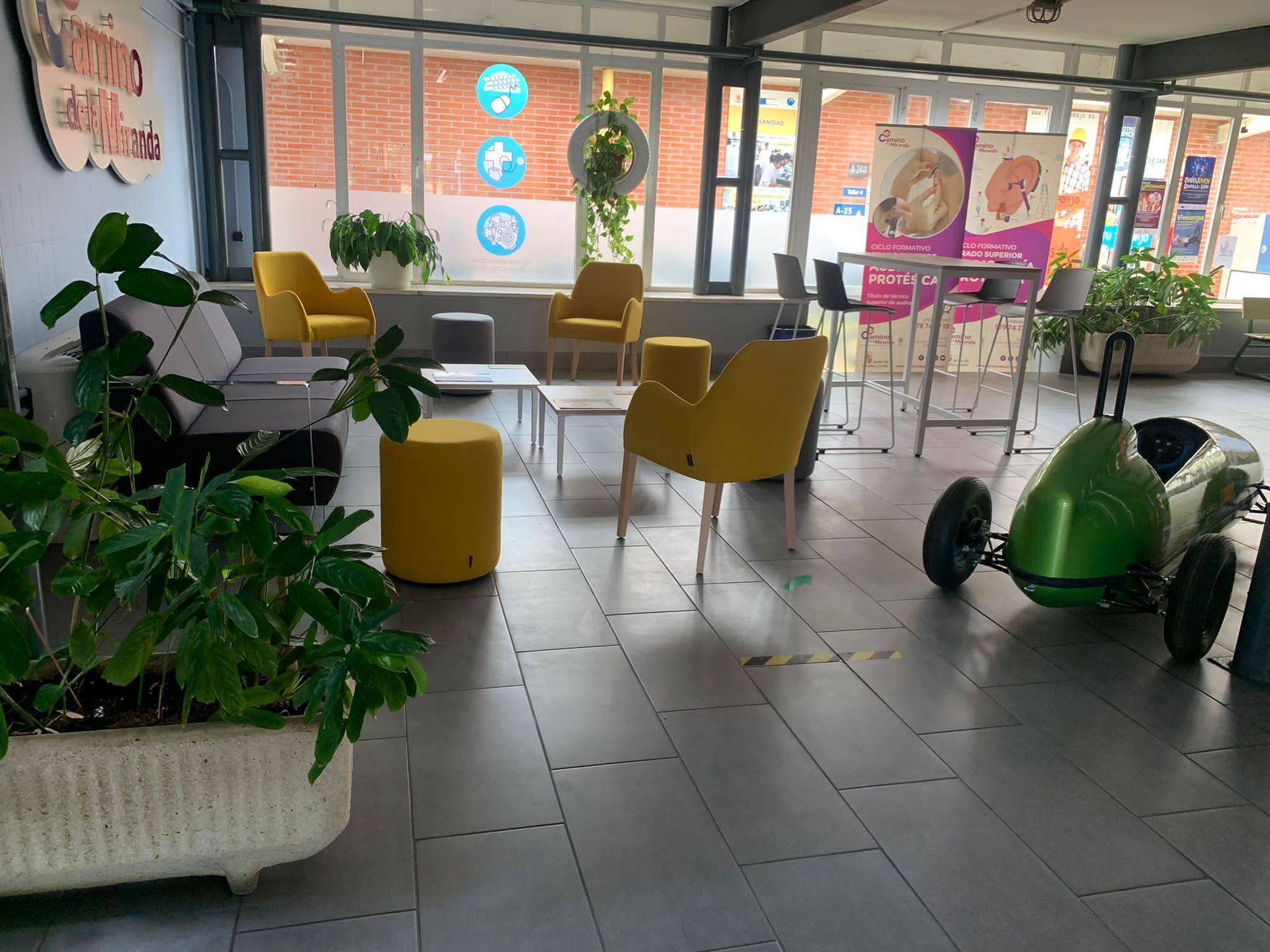 Zona de salón con sillas amarillas, coche verde y grandes ventanales.