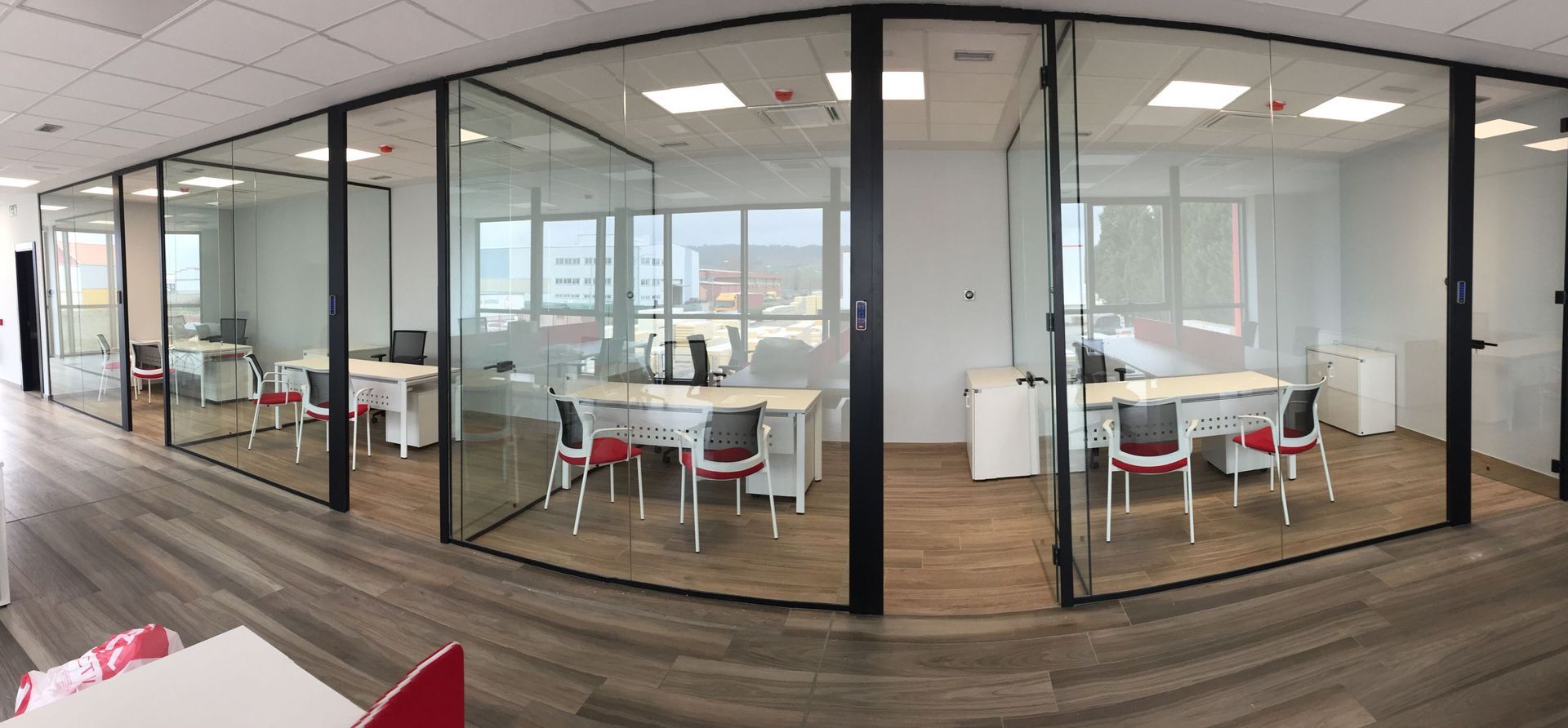 Espacio de oficina con habitaciones con paredes de vidrio, escritorios, sillas y pisos de madera.