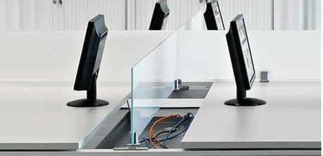 Estaciones de trabajo de oficina con computadoras y mamparas de vidrio.