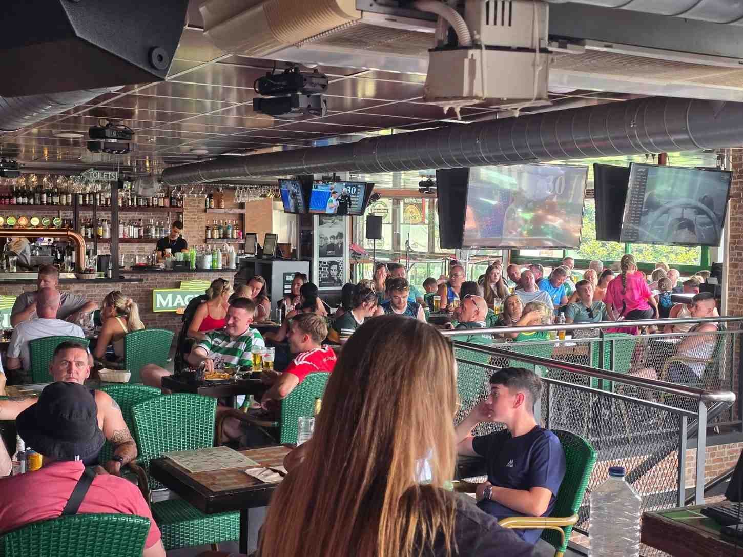 Bar deportivo abarrotado de clientes que ven la televisión en pantallas y beben en las mesas.