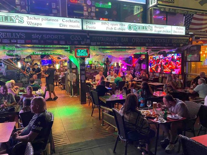 Restaurante al aire libre con coloridas luces de neón y comensales sentados en mesas por la noche.
