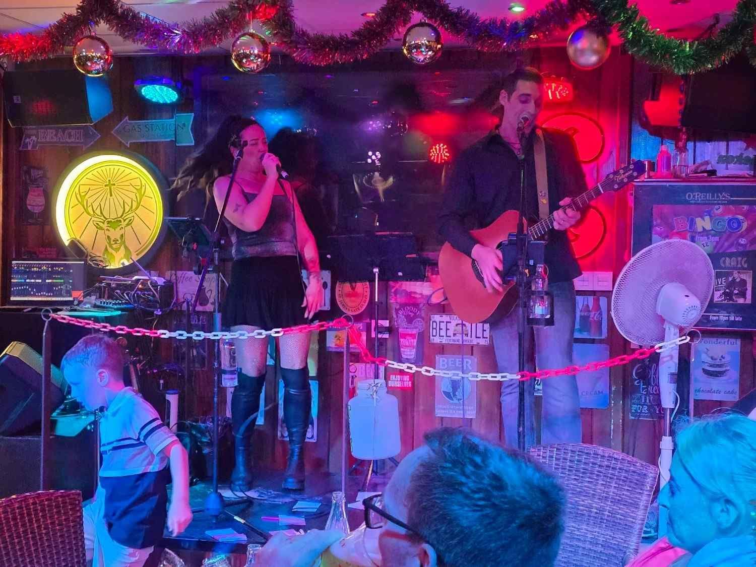 Un grupo musical en vivo actuando en un pequeño escenario con luces rojas y público sentado frente a él.