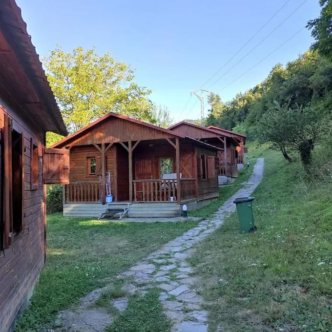Una casa de madera con un bote de basura verde delante de ella.