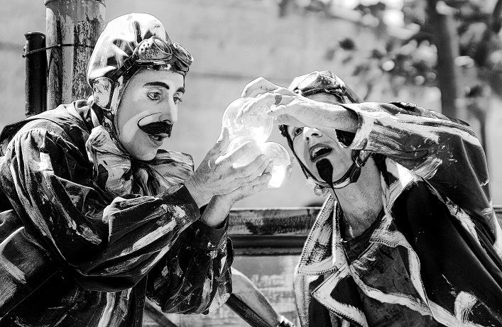 Un hombre con gafas y traje azul se sienta en un espacio iluminado de azul, mirando hacia adelante.