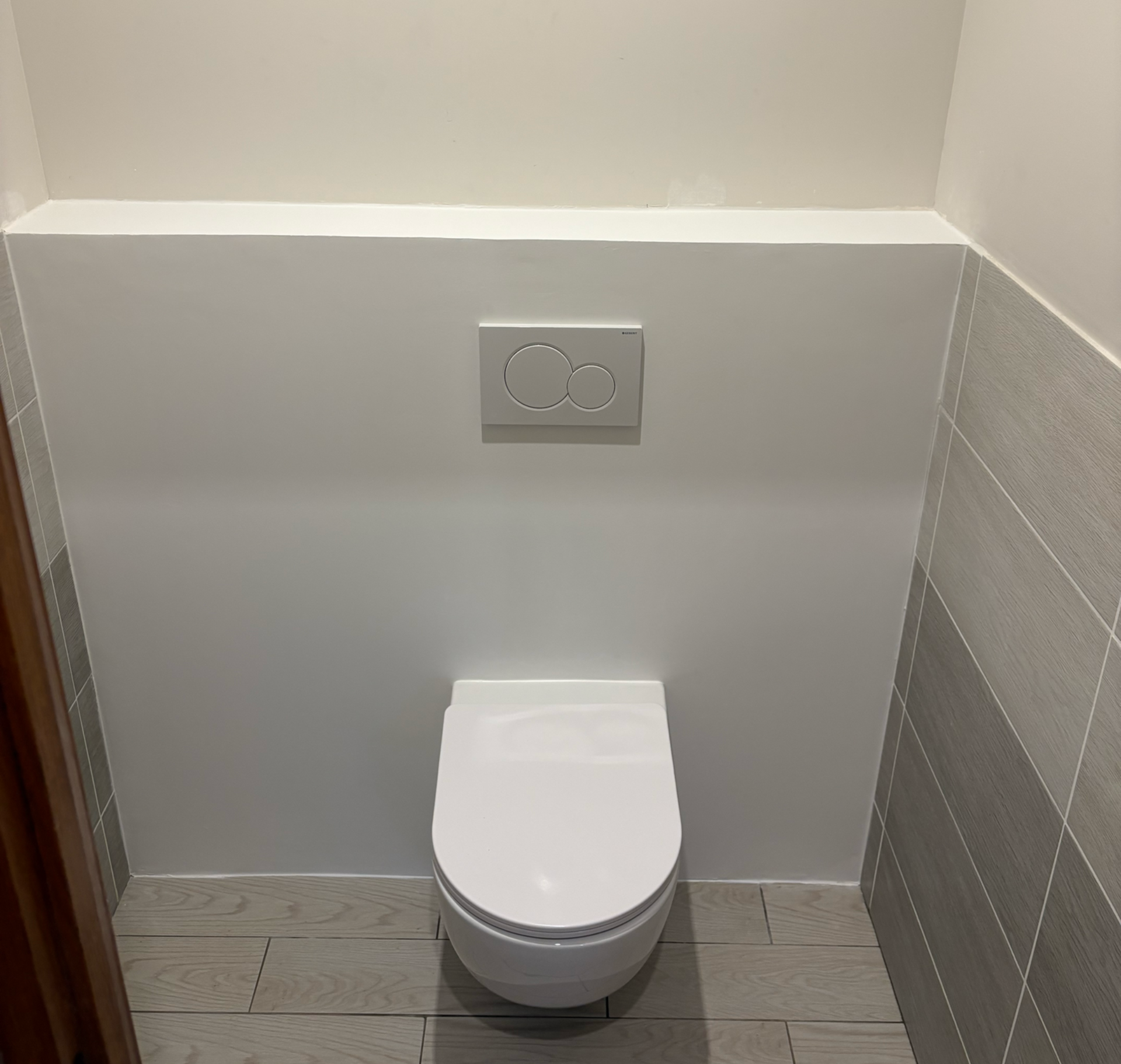 Toilettes murales blanches modernes dans une petite salle de bains carrelée avec un bouton de double chasse d'eau au-dessus
