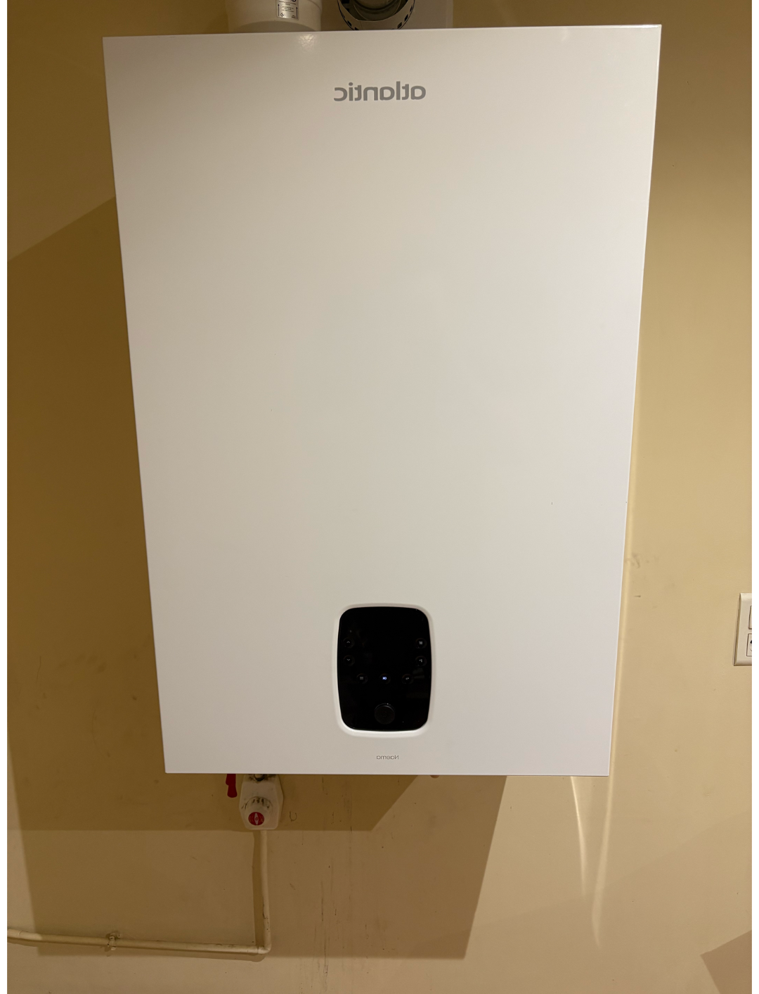 Chaudière ou chauffe-eau mural blanc avec un petit écran noir sur un mur beige.