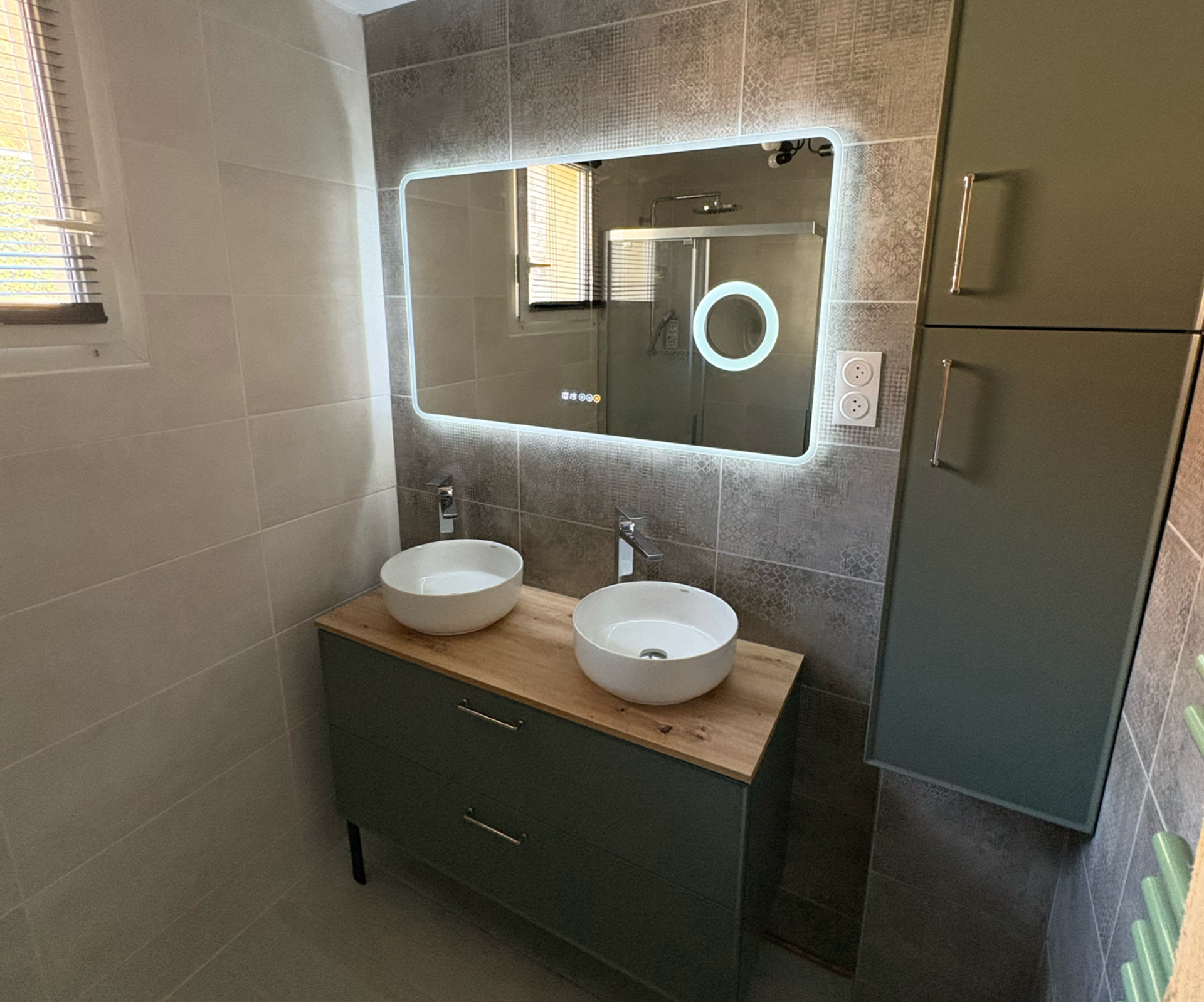 Meuble-lavabo moderne avec deux vasques blanches, miroir rétroéclairé et armoire vert foncé.