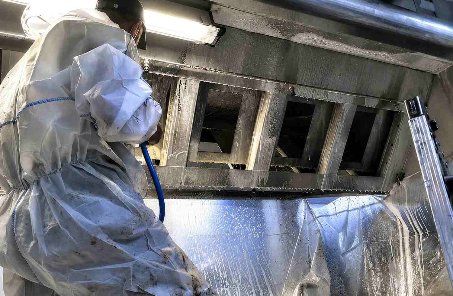 Un trabajador con traje protector rocía el interior de un conducto metálico con desinfectante o pintura.