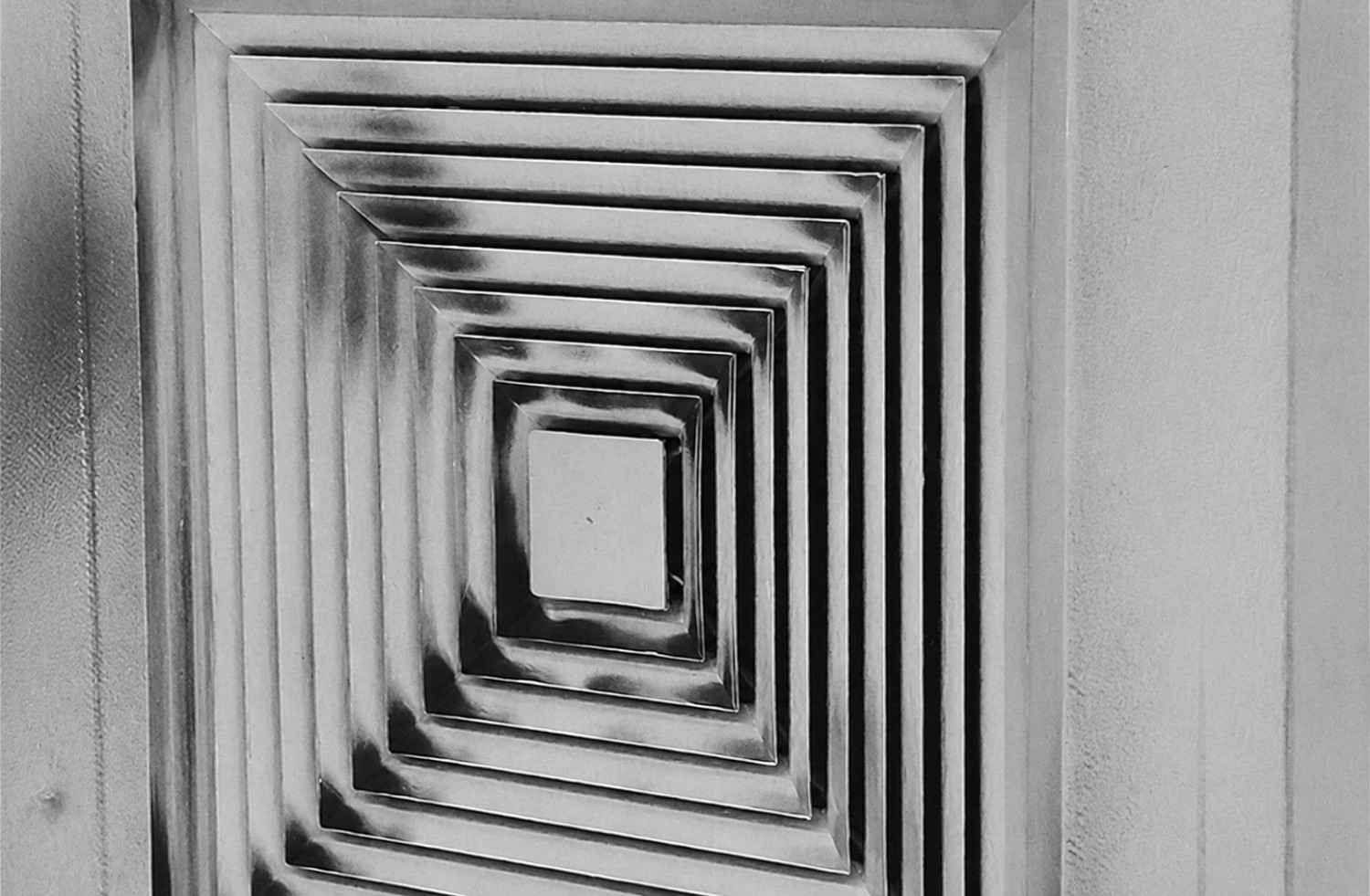 Rejilla de ventilación geométrica en blanco y negro con marcos cuadrados anidados que crean un patrón similar a un túnel.