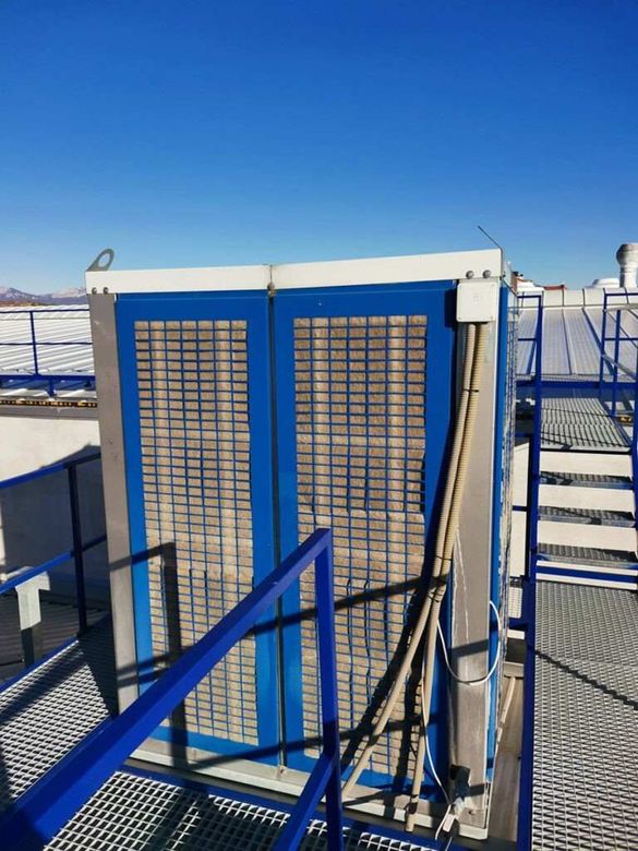 Unidad de climatización azul en la azotea, detrás de barandillas metálicas, bajo un cielo despejado.