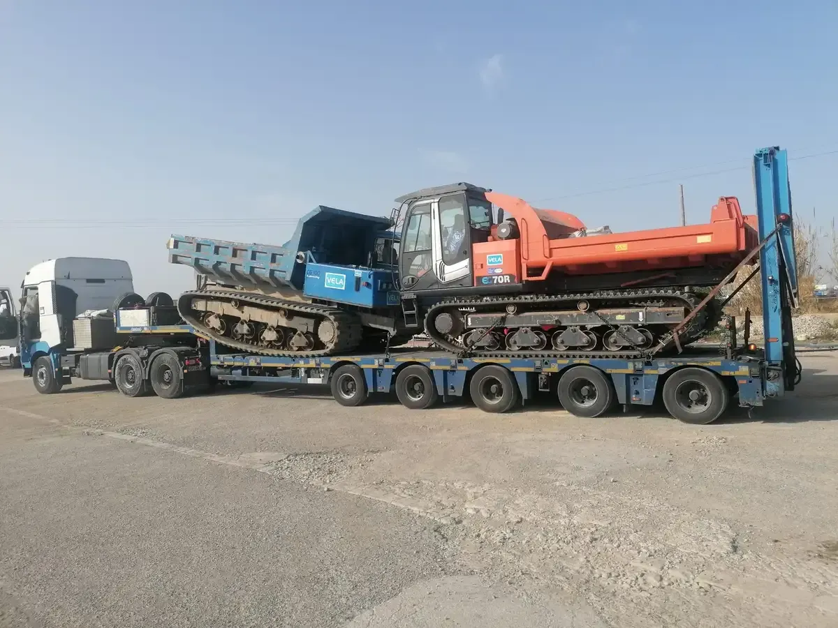 Obreros de la construcción con chalecos naranjas guiando una excavadora en una obra de tierra.