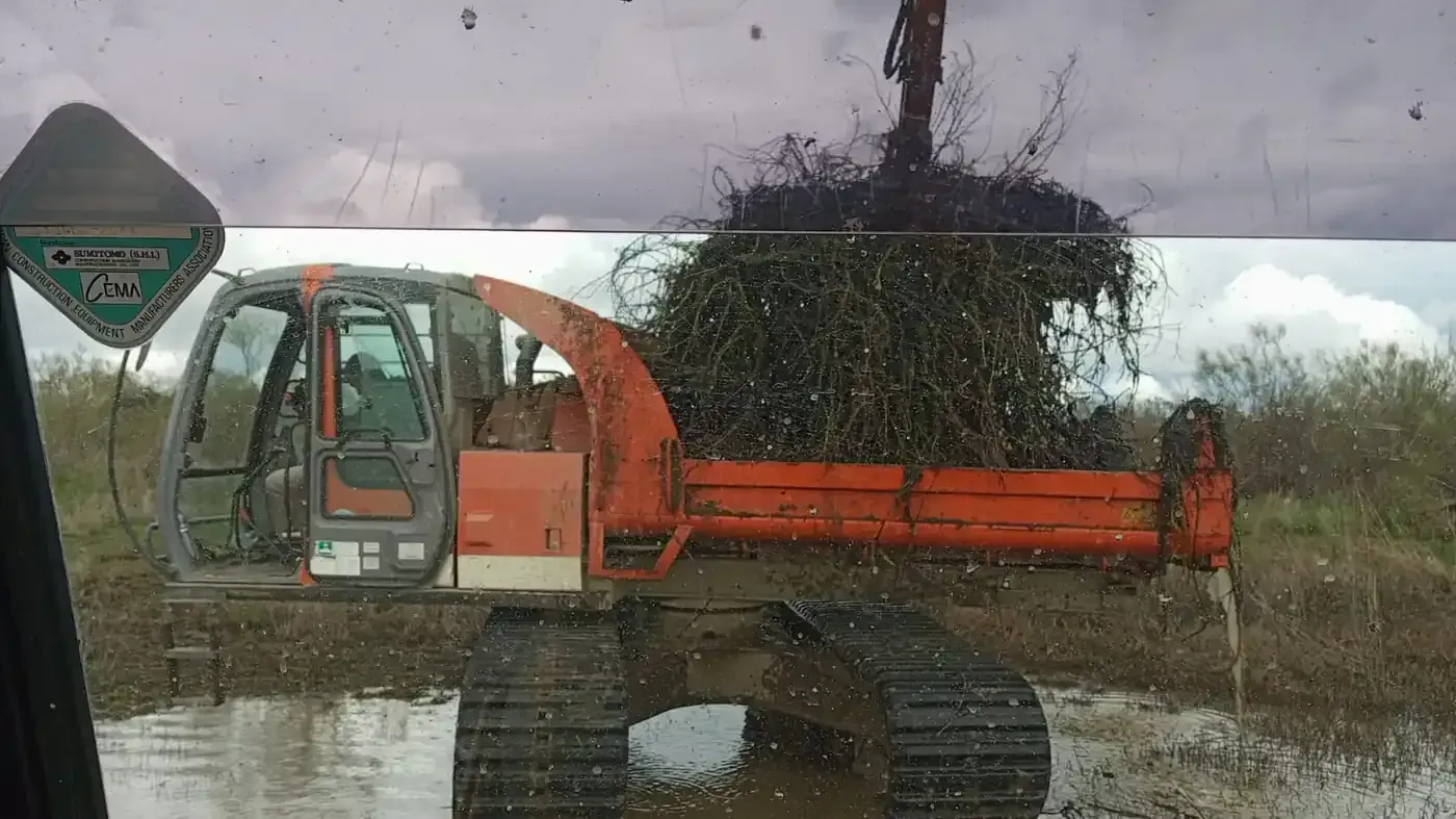 Obreros de la construcción con chalecos naranjas guiando una excavadora en una obra de tierra.