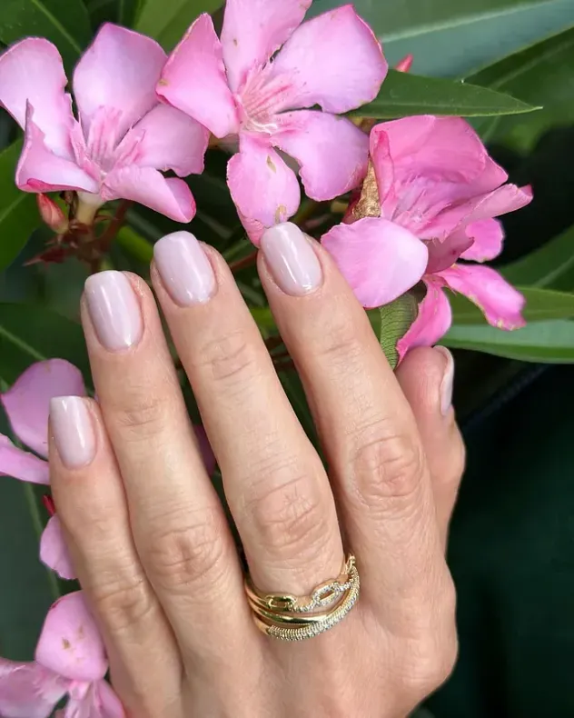 Un primer plano de la mano de una mujer con un anillo y flores rosas en el fondo.