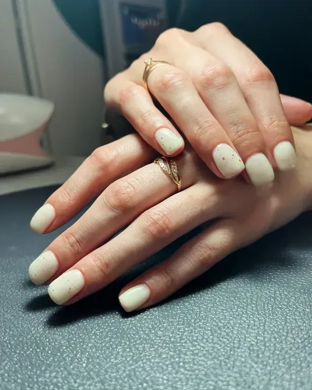 Manos de mujer con uñas blancas y un anillo en el dedo.